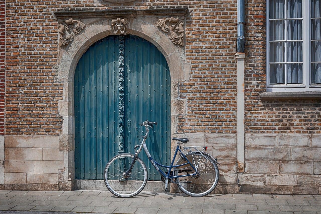 Bicicleta apoyada junto a una puerta verde en una calle de ladrillo